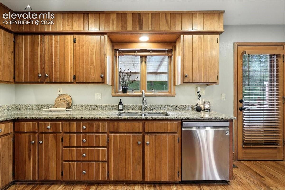 Kitchen featuring vertical-plank cabinetry, stone-surface countertops, a stainless steel dishwasher, an undermount sink with a gooseneck faucet, and wood-finish flooring