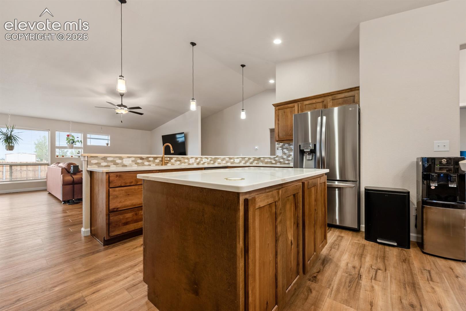Kitchen featuring stained cabinetry, a central island with a solid surface countertop, stainless steel refrigerator, mosaic tile backsplash, and wood-finish flooring