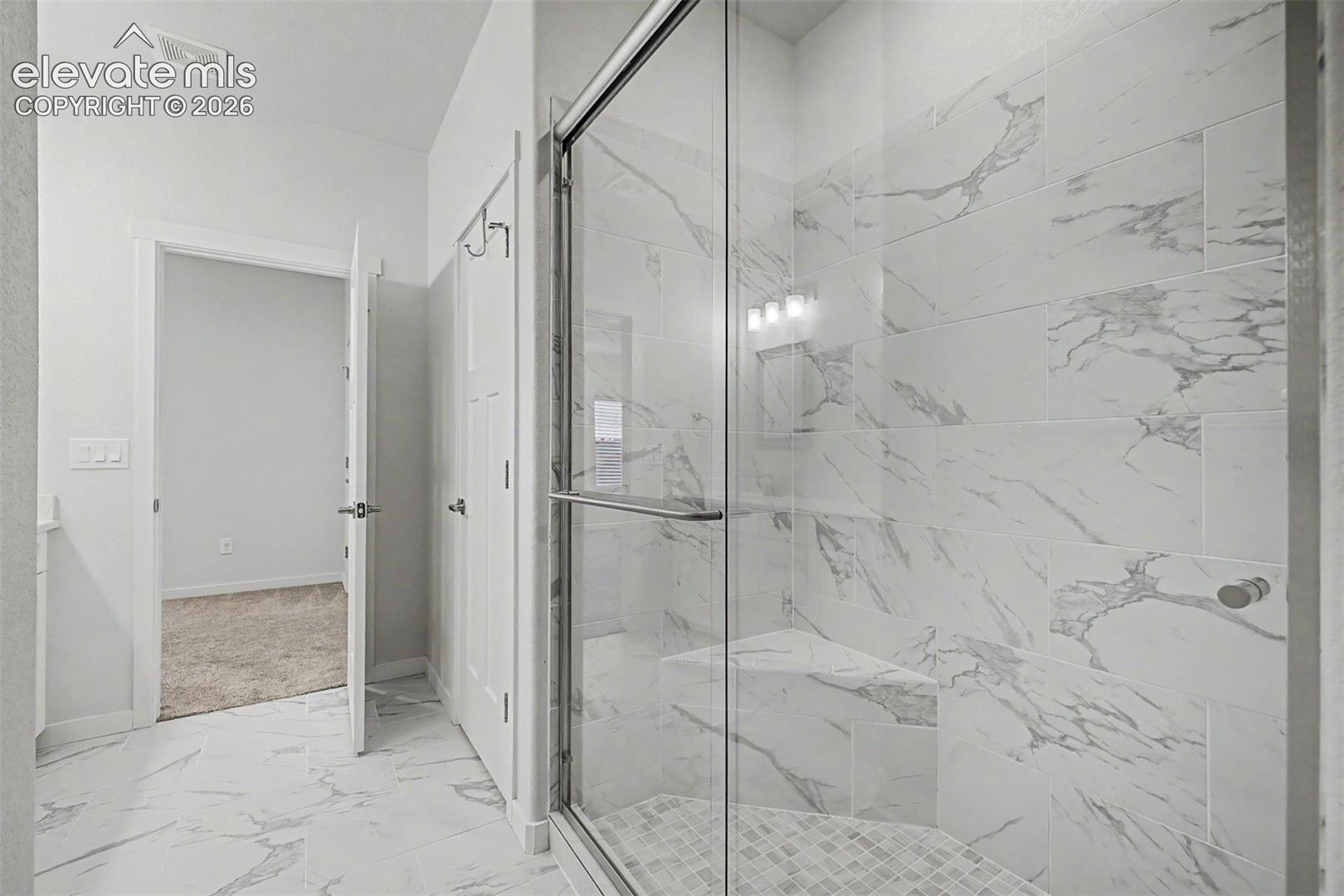 A floor-to-ceiling marble-look tile walk-in shower with a built-in bench and frameless glass enclosure transforms the daily routine into something approaching a spa experience — this is where the day begins and ends beautifully.