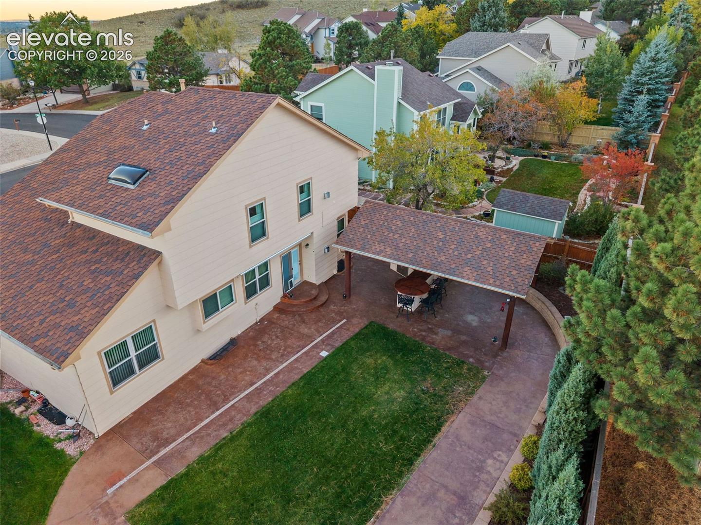 Multi-level exterior featuring a shingled roof with a skylight, covered rear patio, stamped concrete hardscaping, and a detached storage shed