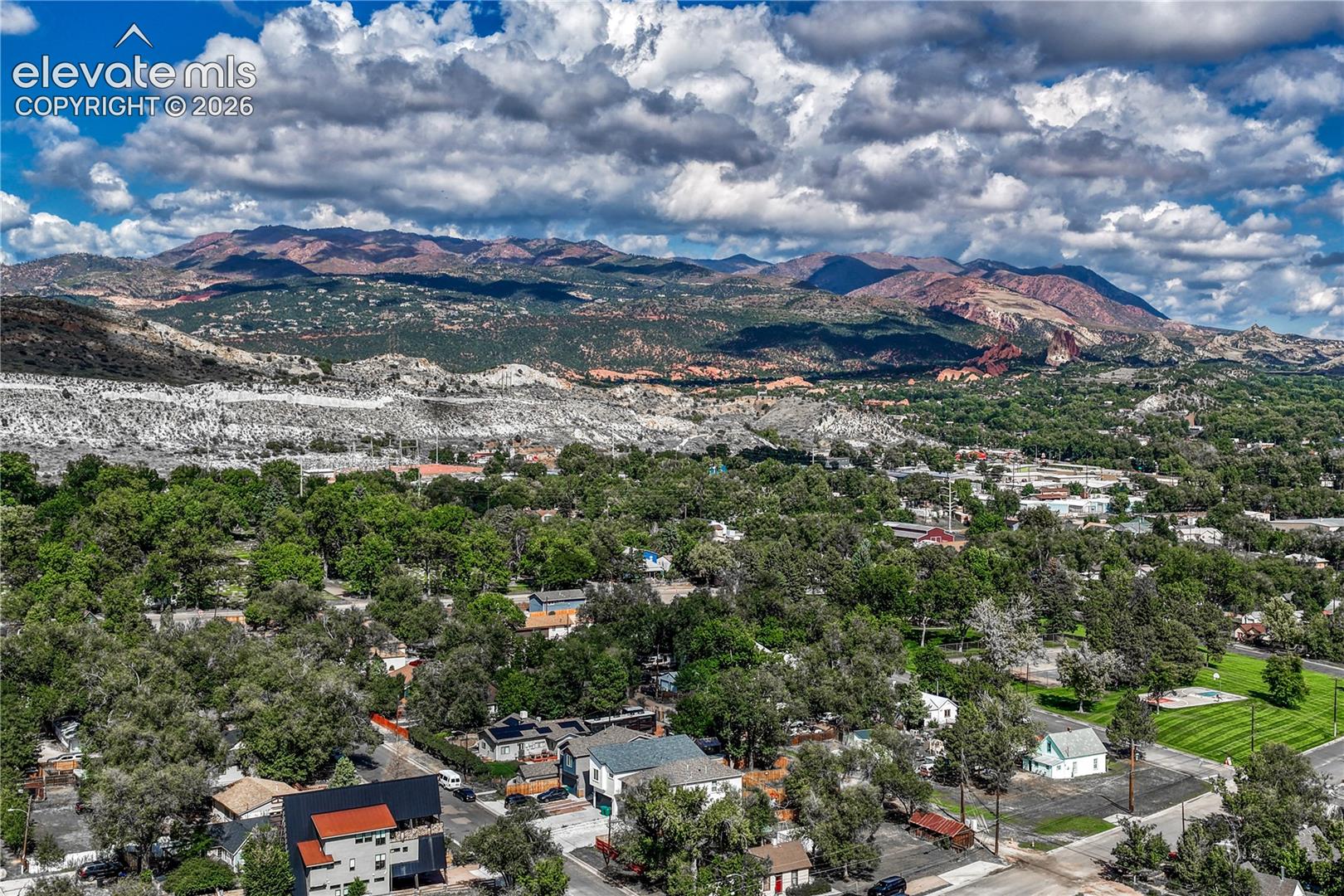 Expansive tree-lined neighborhood with distant mountain ranges and scattered residential structures