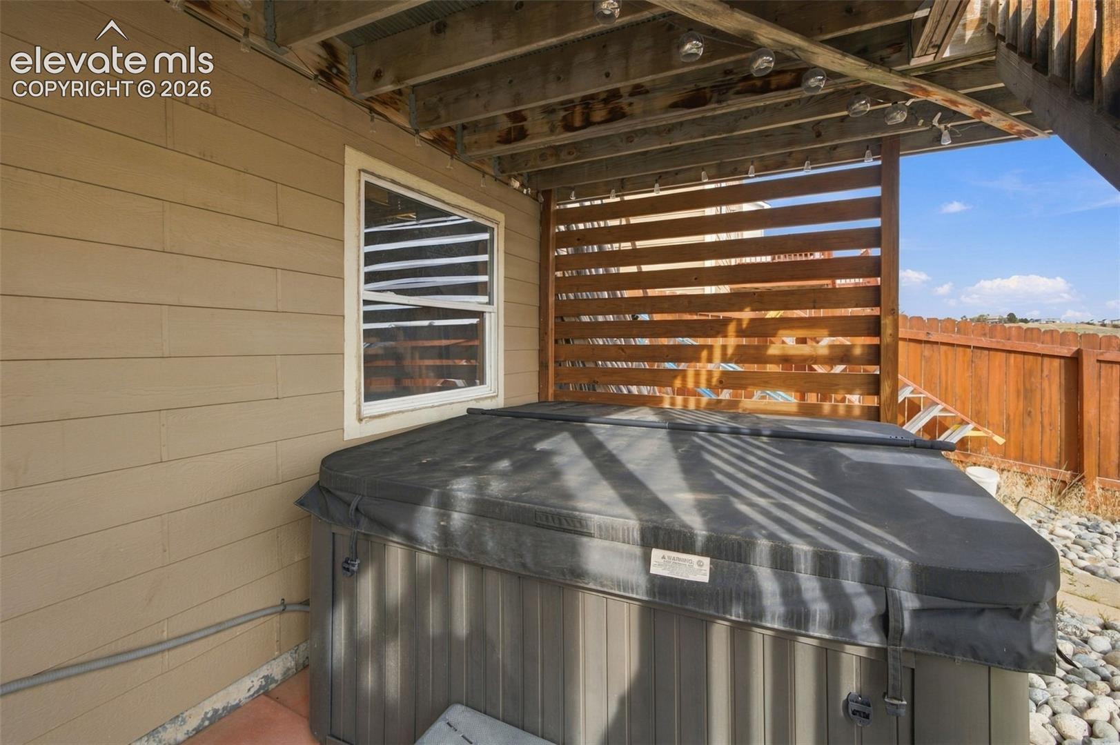 Covered patio area featuring a built-in hot tub, horizontal wood privacy screening, and stone ground cover