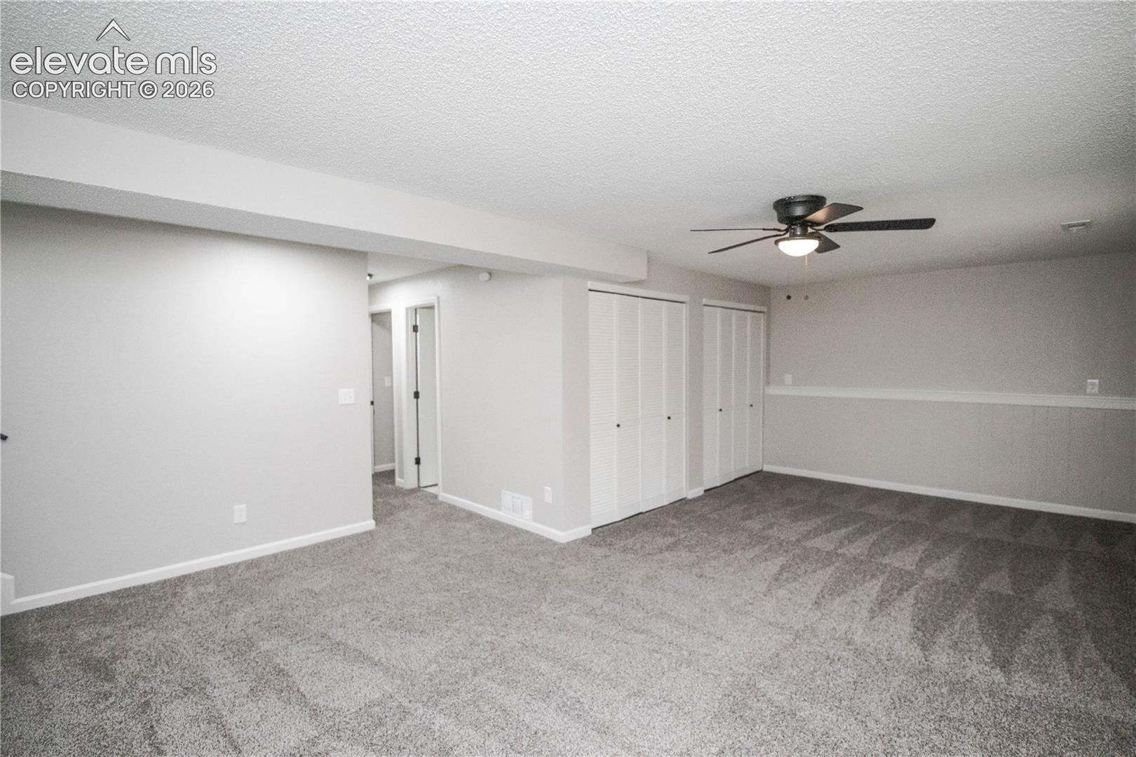 Neutral-toned interior featuring wall-to-wall carpeting, chair rail molding, two sets of bifold closet doors, and a ceiling-mounted light fixture with fan