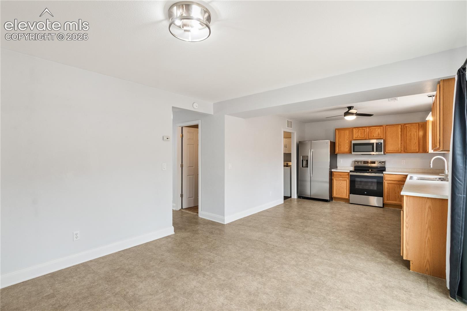 Kitchen featuring wood cabinetry, stainless steel appliances, a ceiling-mounted fan, and continuous flooring