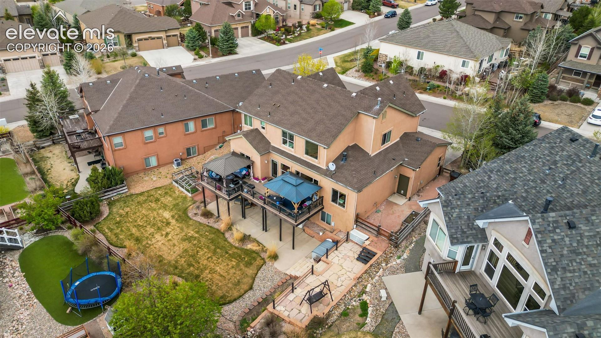 Expansive backyard featuring a large raised deck, multi-level flagstone patio, sloped lawn area, mature landscaping, and an artificial turf section