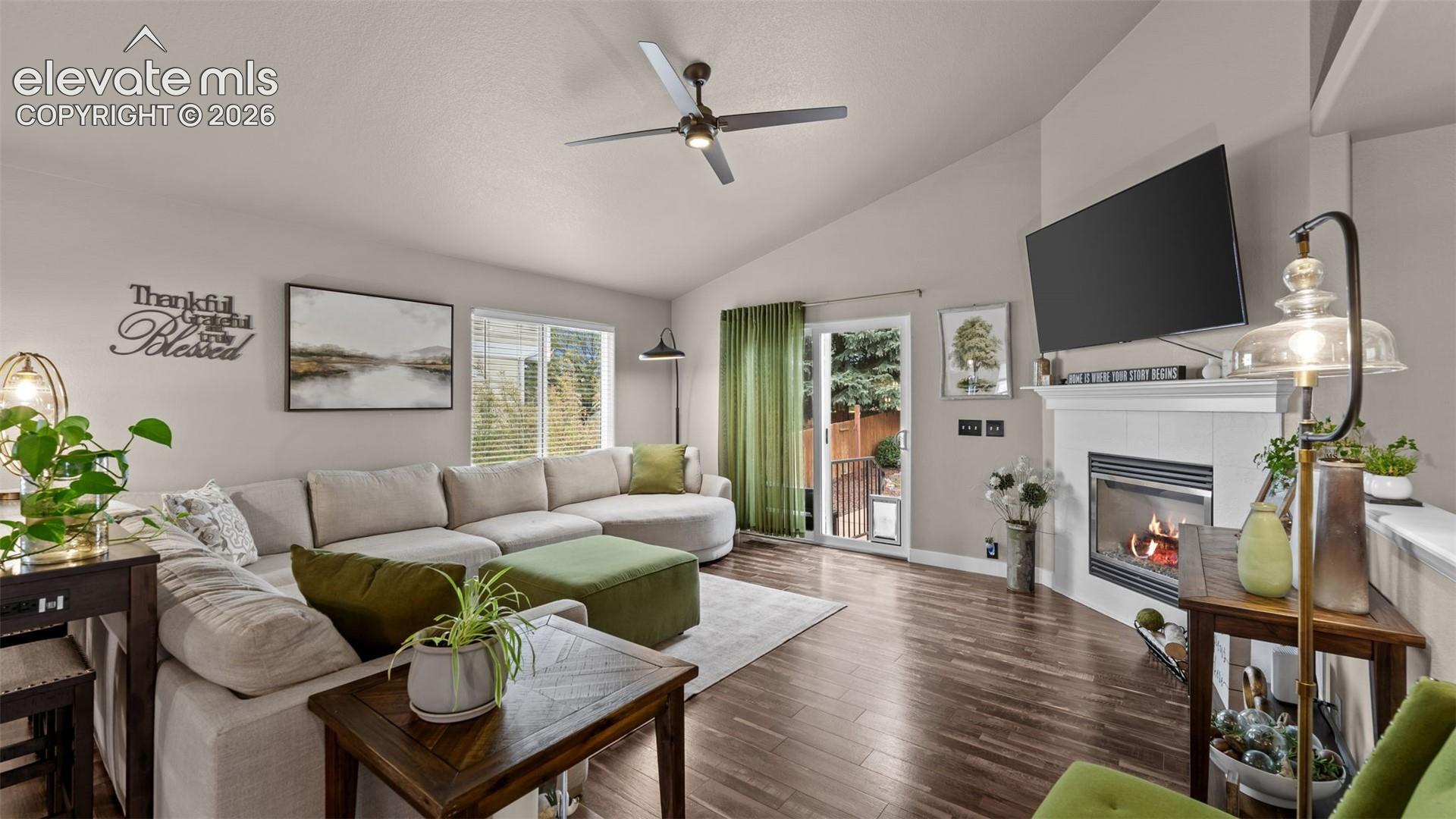 Living room featuring vaulted ceilings, wood-finish flooring, a fireplace with a white mantel, and a ceiling fan