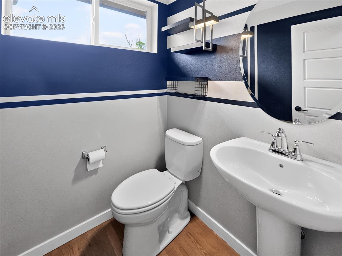 Pedestal sink with chrome faucet set against a contemporary wall design, featuring wood-finish flooring and a horizontal transom window half bath off kitchen next to laundry