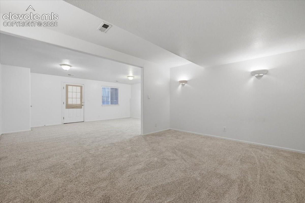 Expansive carpeted area with recessed lighting, wall sconces, and a window with security bars