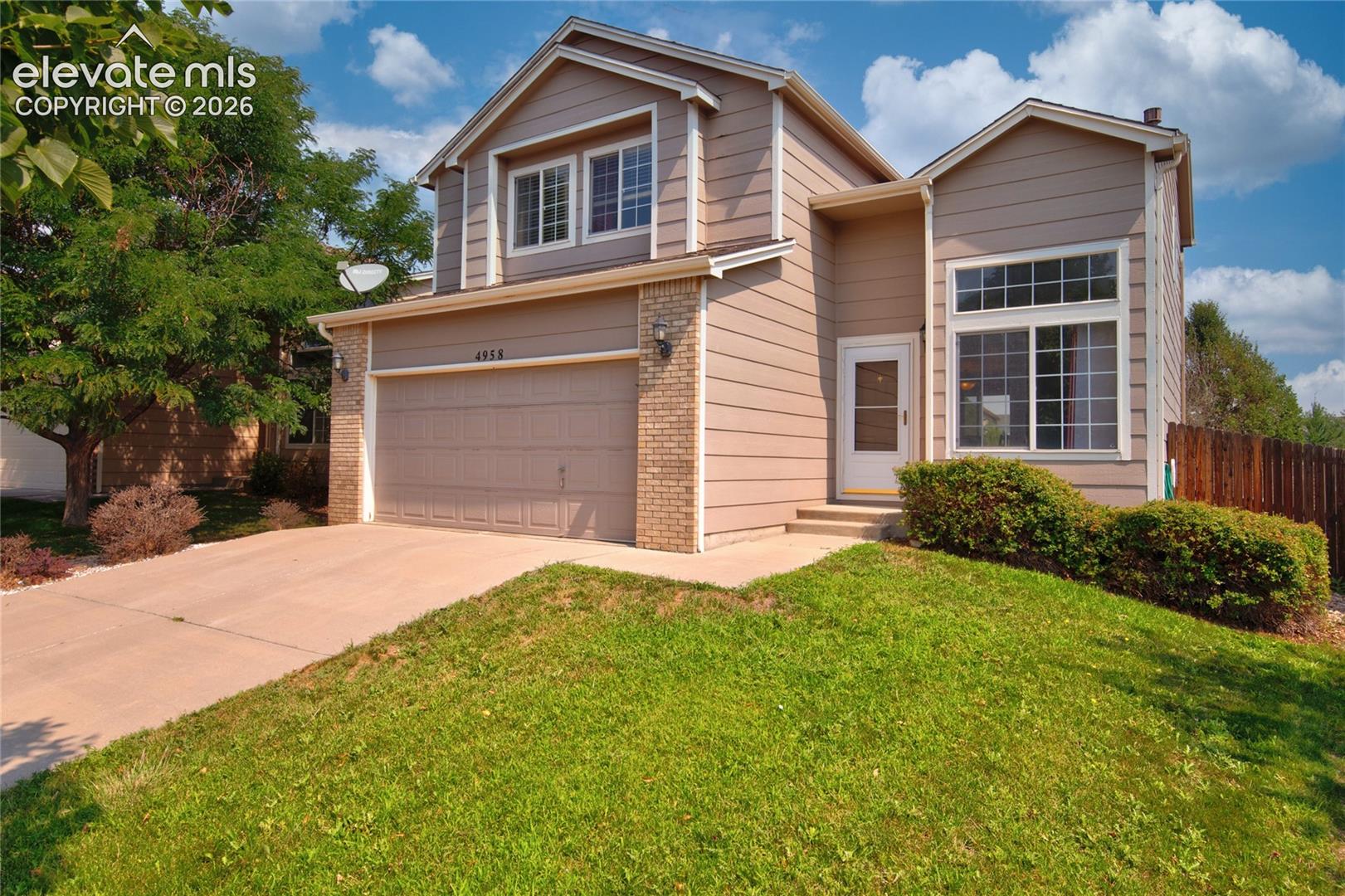 Two-story property featuring a front-facing garage, brick accents, and a concrete driveway