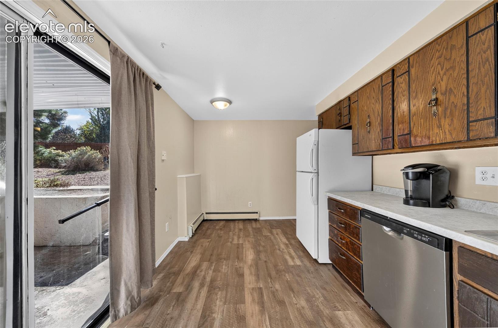 Kitchen featuring wood-finish cabinetry, neutral countertops, stainless steel dishwasher, wood-finish flooring, and sliding glass door access to an outdoor patio