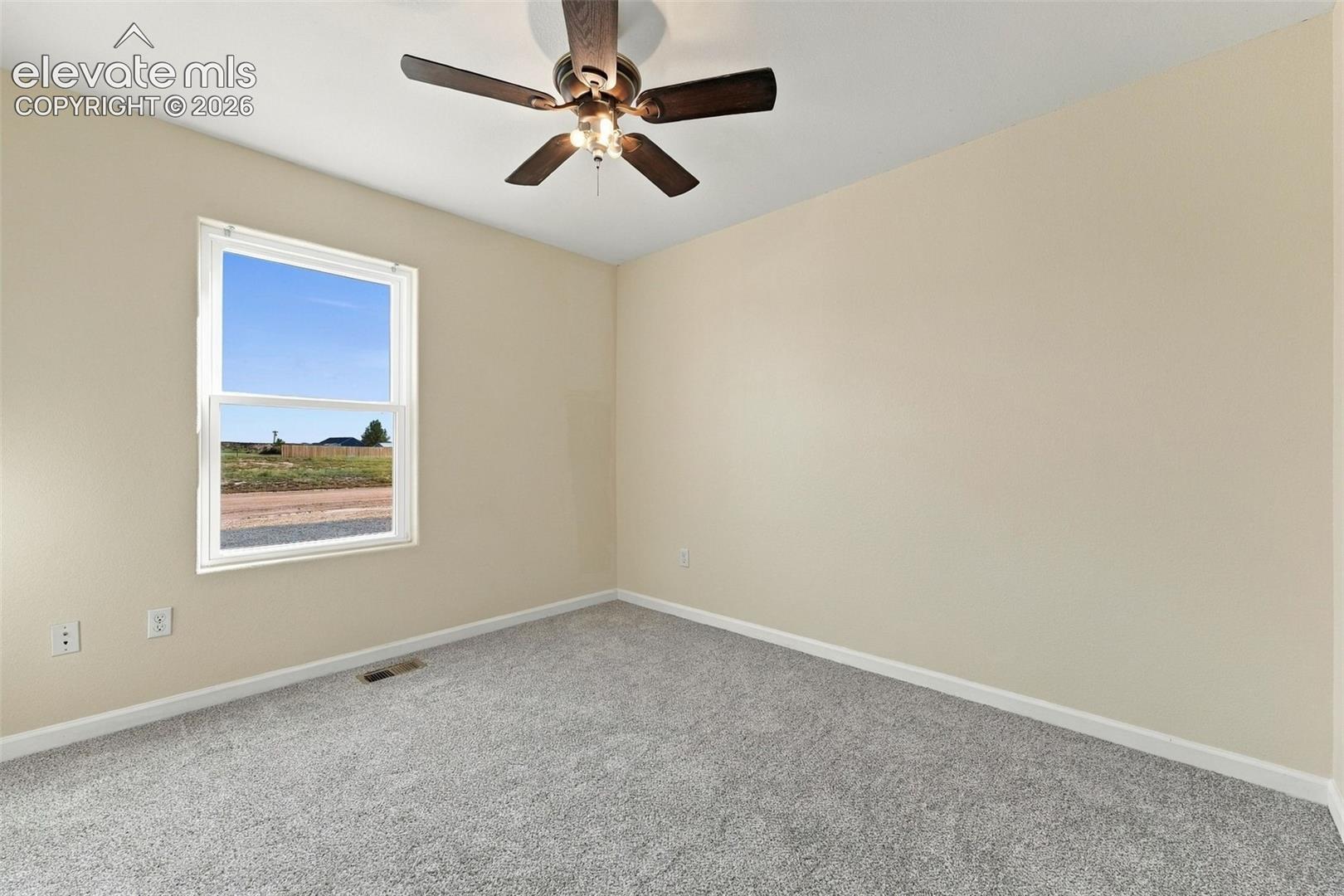 Neutral-toned walls, high-pile carpeting, and a ceiling fan with integrated light fixture, featuring a single-hung window with exterior landscape exposure