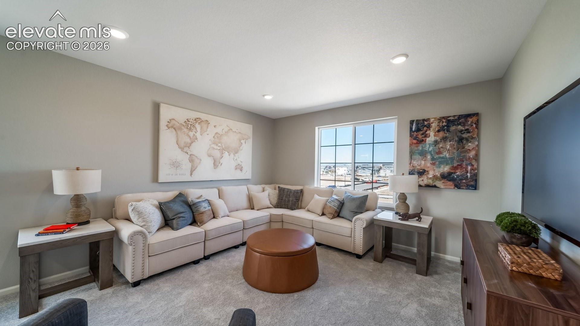 Recessed lighting, large window with grid pattern, light gray wall paint, light-colored carpet, and dark wood-finish media console
*photos of a model home*