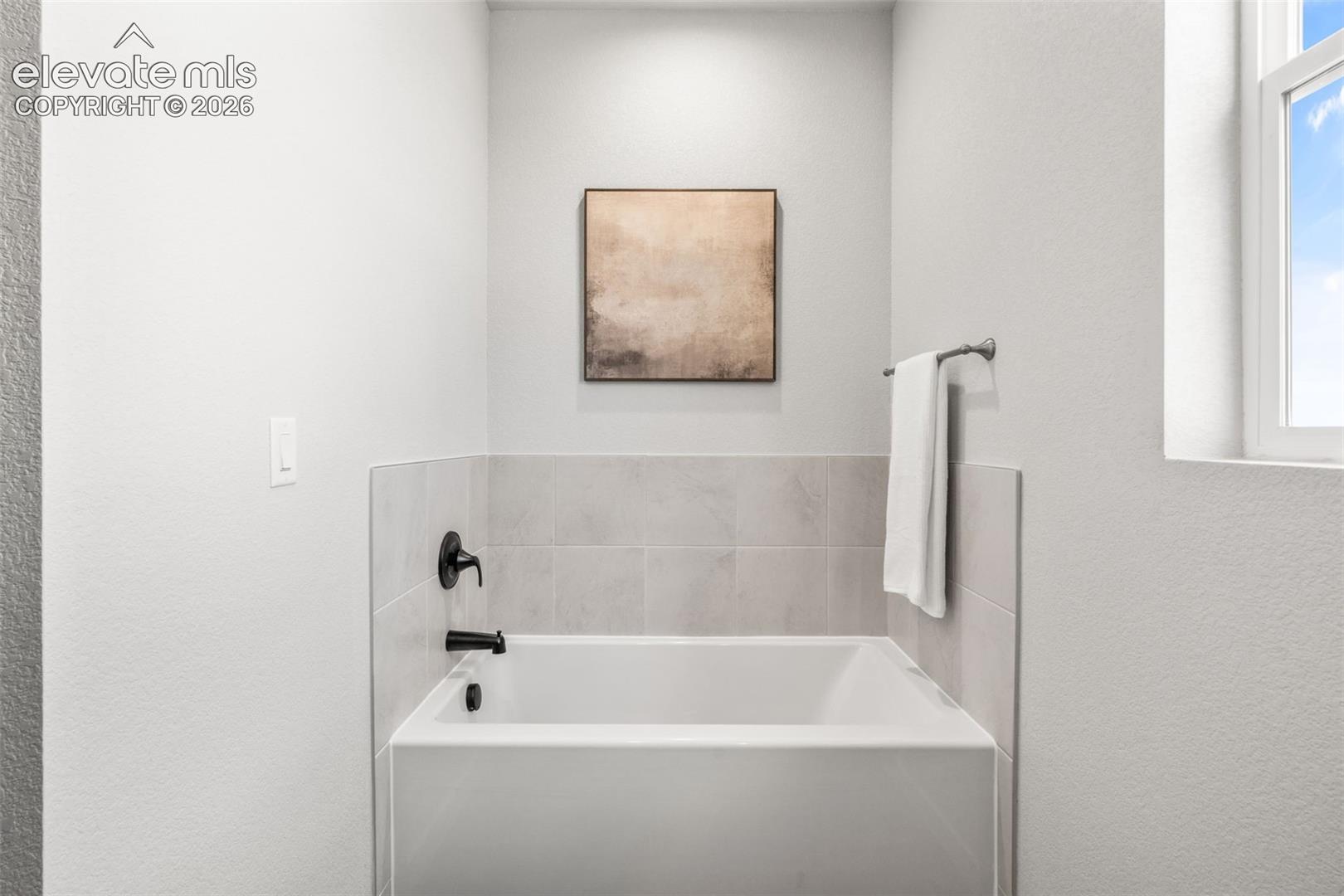 Bathtub with matte black fixtures, light-toned wall tile surround, and a window