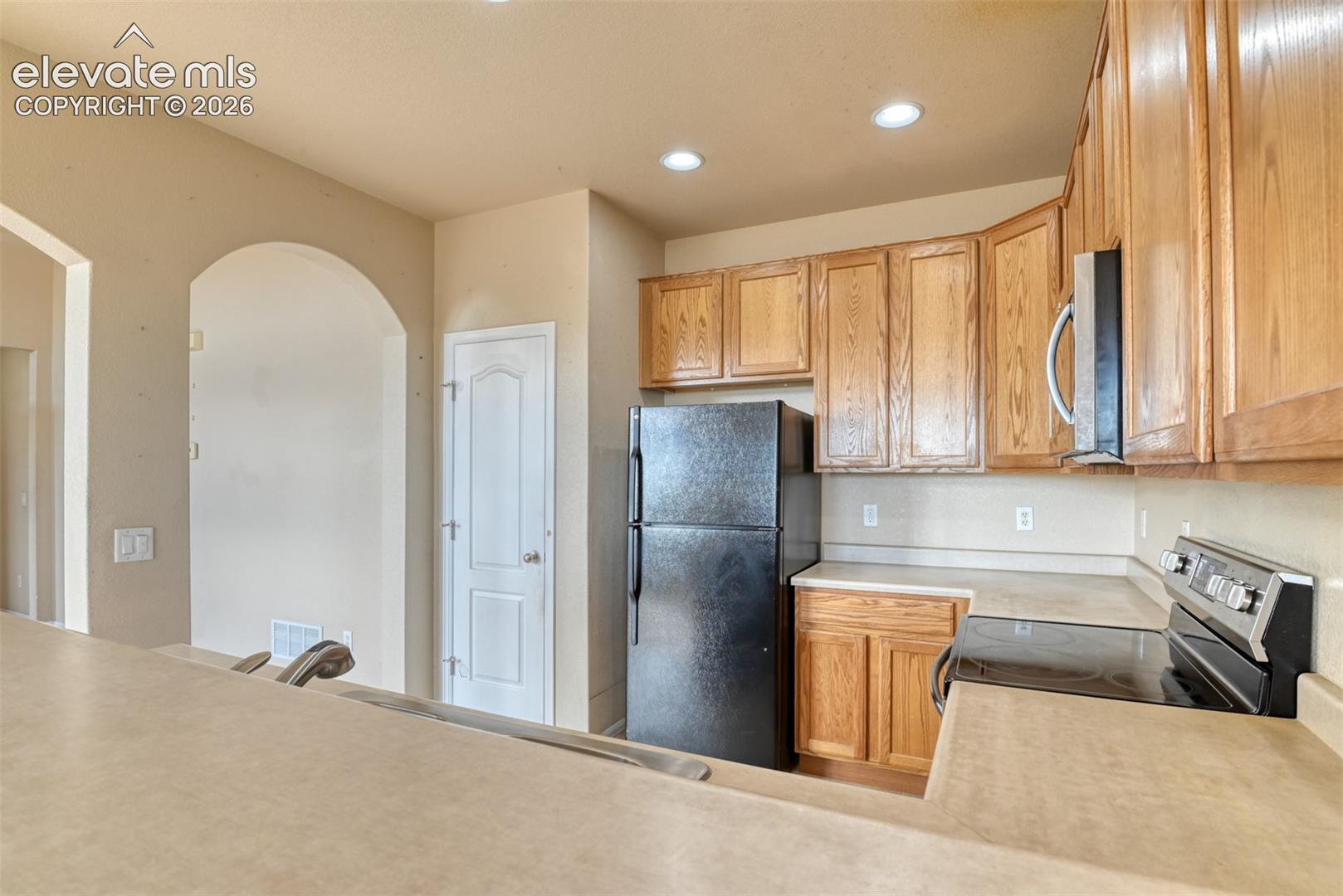 Kitchen featuring stained wood cabinetry, solid-surface countertops, recessed lighting, and a prominent arched entryway