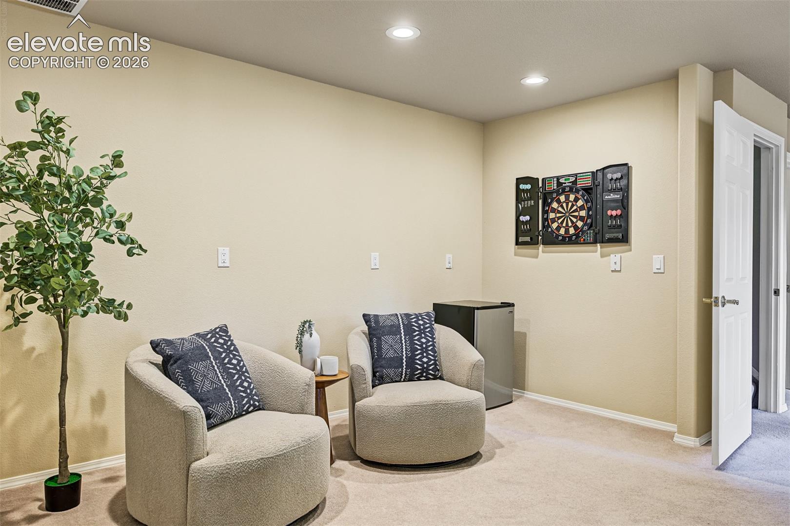 Flexible sitting nook or workspace in the full walkout basement, featuring recessed lighting, neutral carpeting, and multiple elevated electrical outlets along the walls for convenient equipment or entertainment setup.