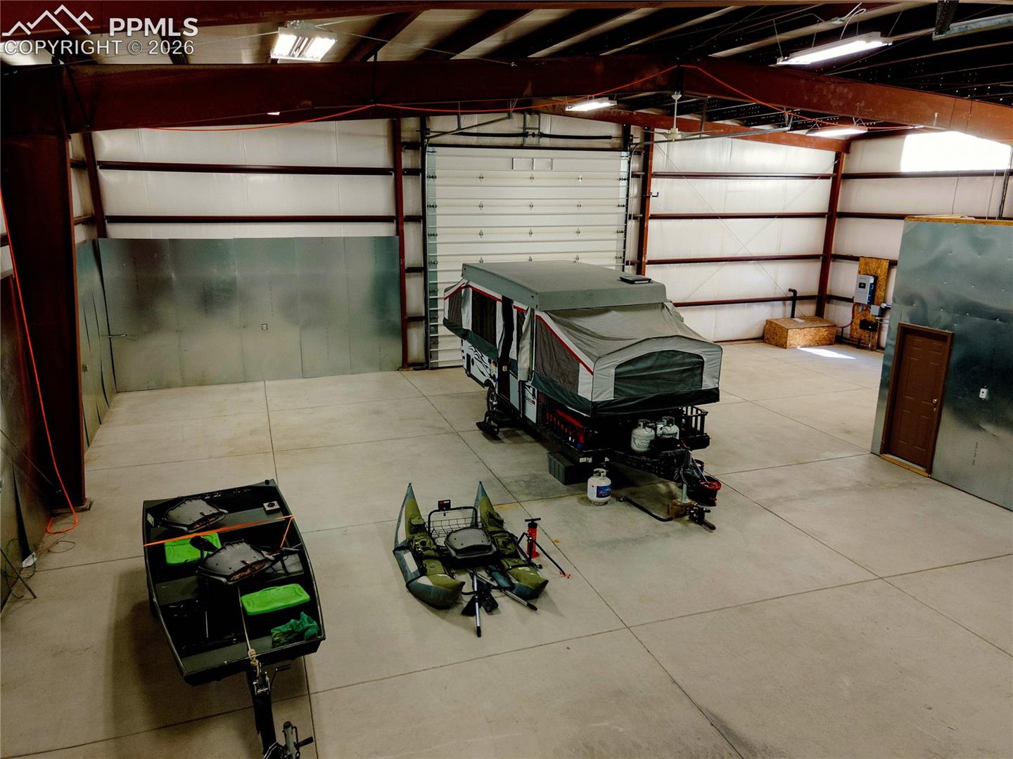 Spacious interior featuring a concrete floor, high ceilings with exposed beams, and a large overhead door