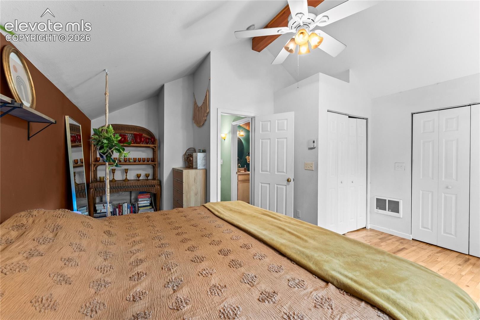 Vaulted ceiling featuring an exposed wood-finish beam, light-tone wood-finish flooring, and a ceiling fan with integrated lighting