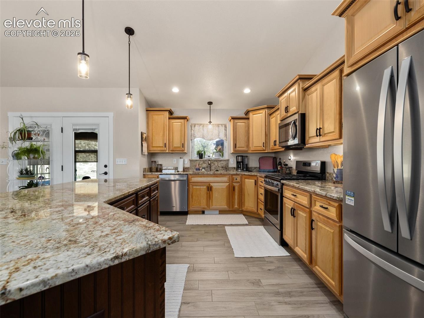 Kitchen featuring light wood-finish cabinetry, stainless steel appliances, granite countertops, and wood-finish flooring