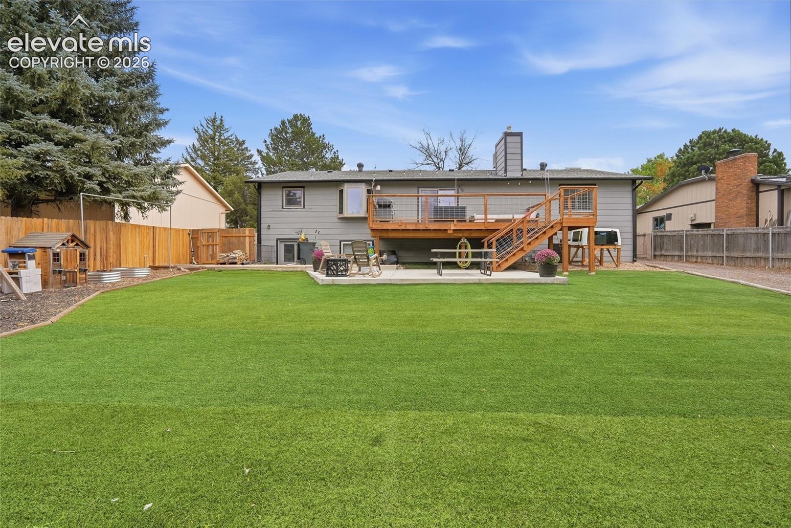 Expansive artificial turf lawn with a multi-level wood deck featuring wood railings and metal balusters