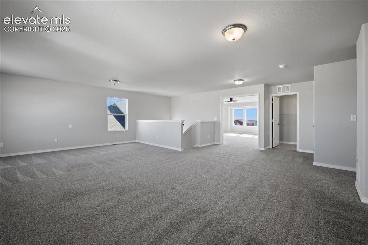 Expansive interior featuring neutral wall tones, wall-to-wall carpeting, flush-mount light fixtures, and a half-wall balustrade