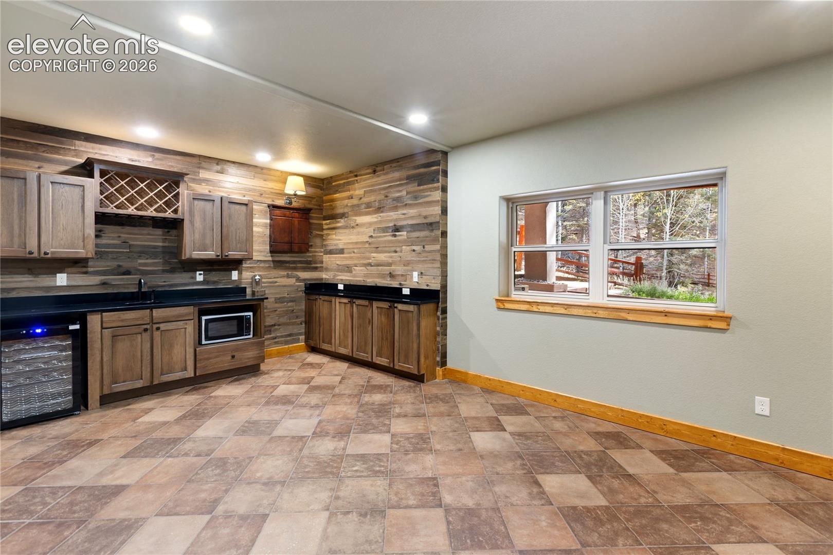 Reclaimed wood plank wall accents, built-in cabinetry with integrated wine refrigeration, stone-tile flooring, solid-surface countertops, and recessed lighting