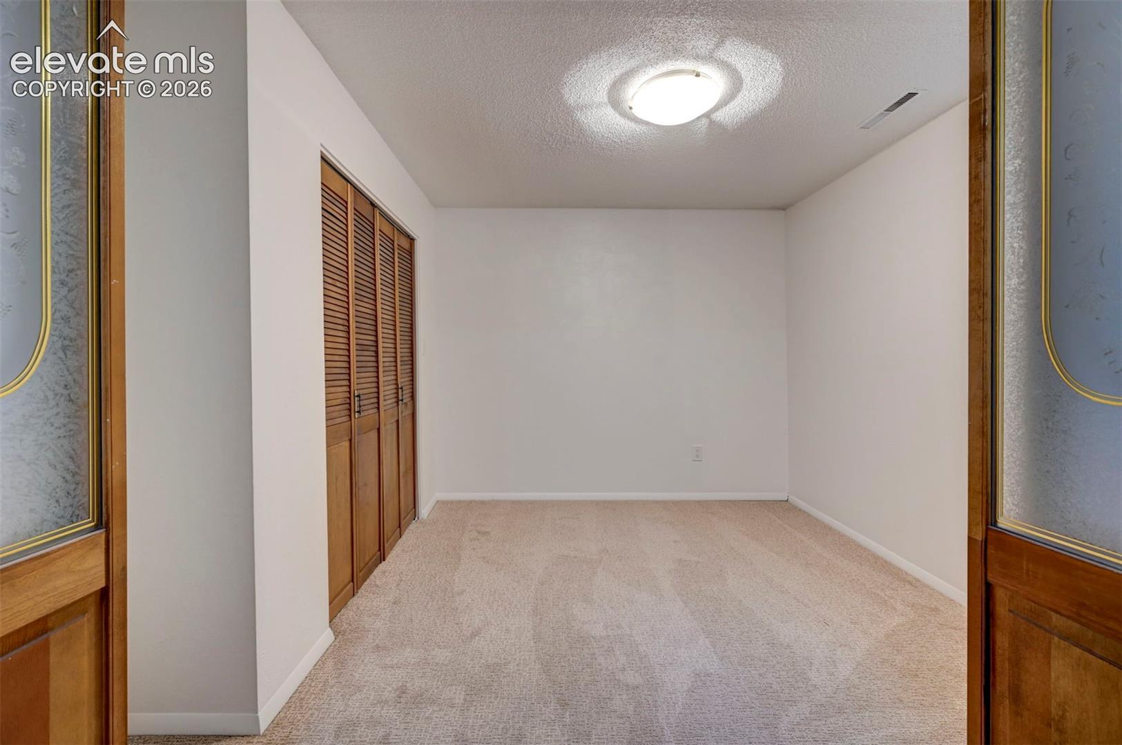 Interior space featuring neutral wall tones, wall-to-wall carpeting, wood-finished louvered closet doors, and wood-framed doors with decorative glass inserts
