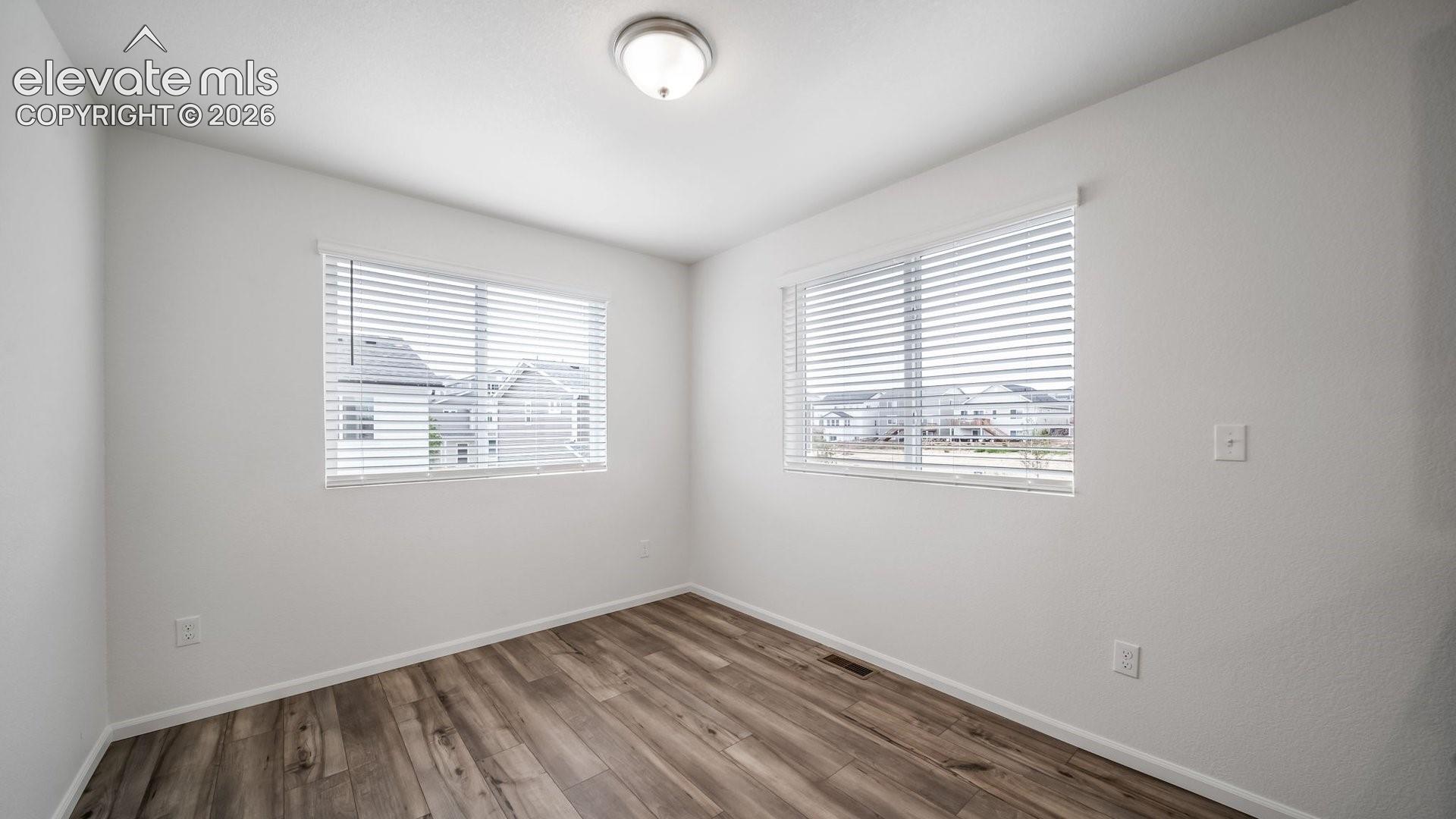 Wood-finish flooring, white walls, two windows with blinds, and a flush mount ceiling light
*photos of a model home*