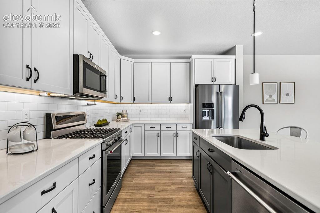 Modern kitchen featuring white shaker cabinetry, stainless steel appliances, a subway tile backsplash, light-toned countertops, and wood-finish flooring