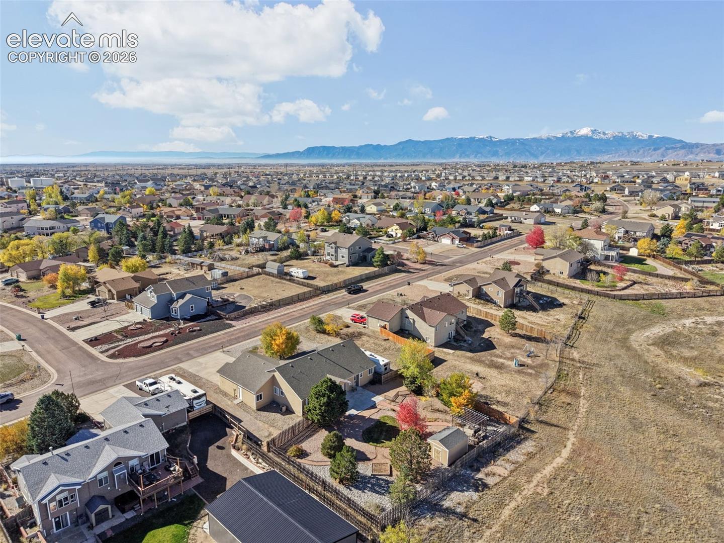 Aerial perspective featuring a multi-level suburban residence with a fenced backyard, mature trees, and a mountain range backdrop