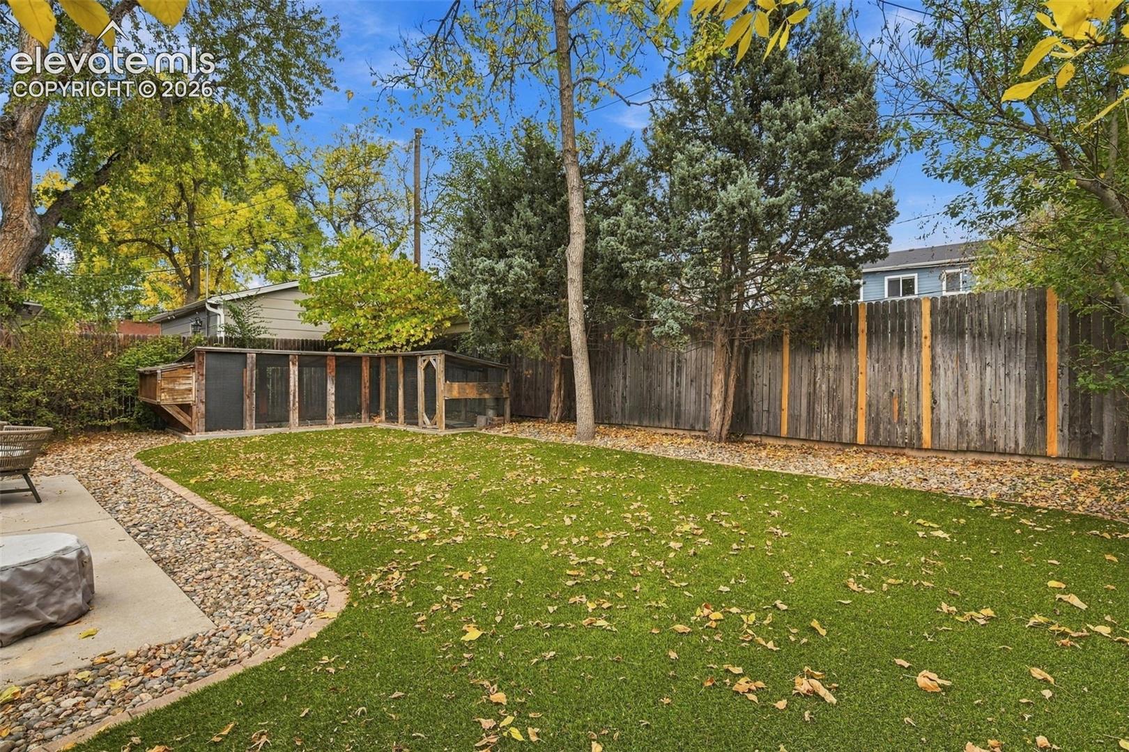 Backyard featuring a synthetic turf lawn, concrete patio, decorative stone border, vertical wood privacy fencing, and a built-in enclosure