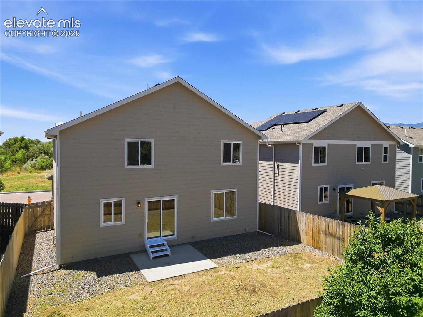 Rear exterior featuring tan siding, a concrete patio, and a sliding glass door