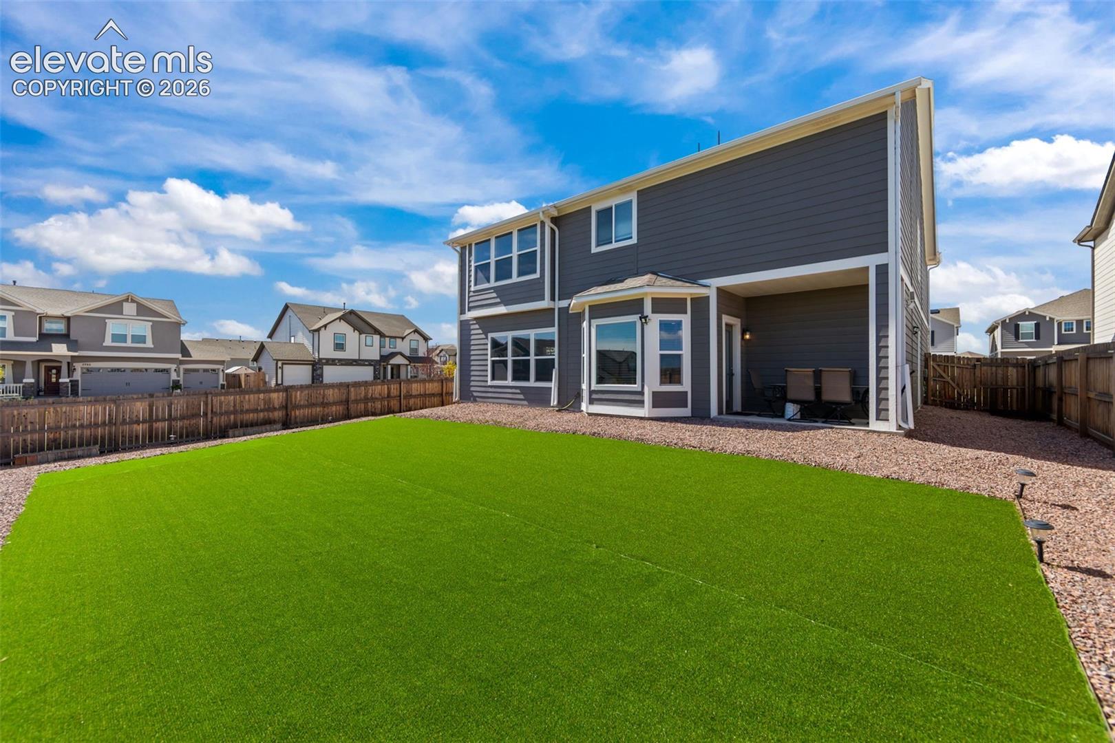 Fenced backyard with artificial turf, gravel pathways, covered patio, and multi-pane windows