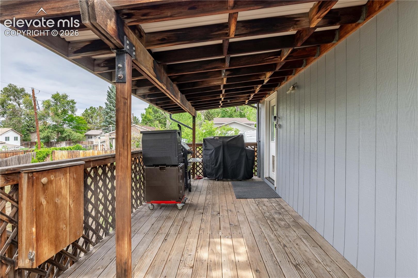 Covered wood deck featuring a lattice railing, exposed beam ceiling structure, and vertical siding