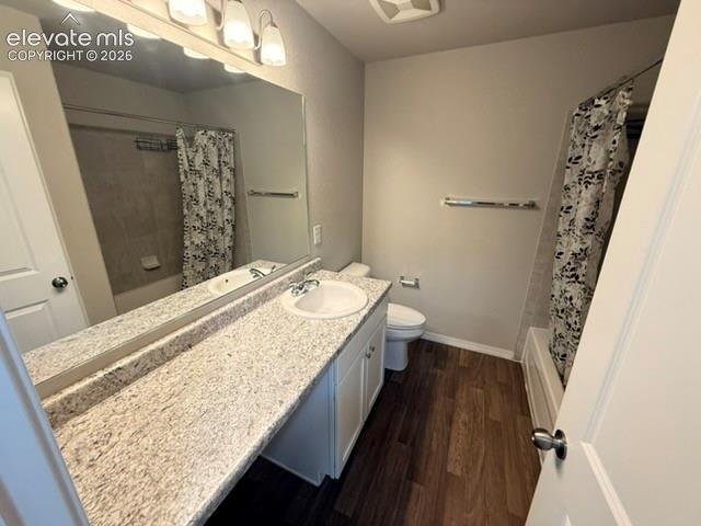 Bathroom featuring a spacious vanity with an integrated sink, expansive mirror, elegant light fixture, and wood-finish flooring