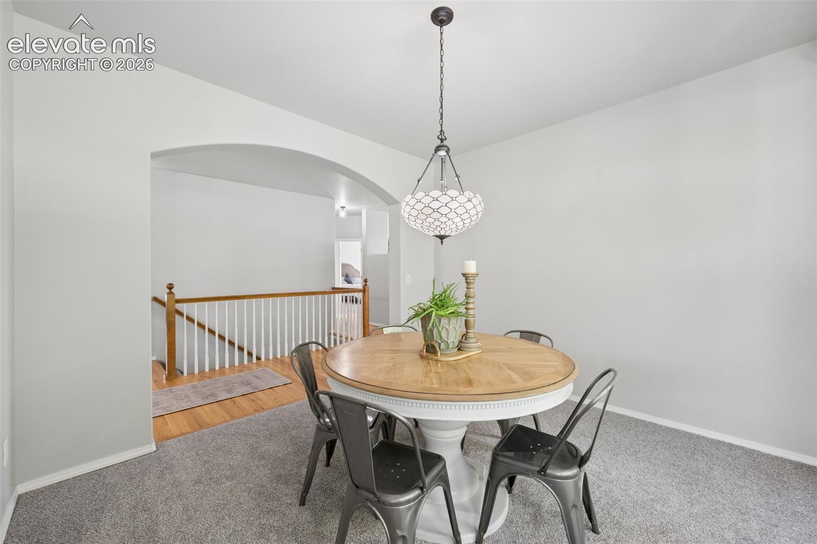 Neutral-toned room featuring a decorative lantern-style pendant light, an arched opening, and wood-finish handrail with white balusters