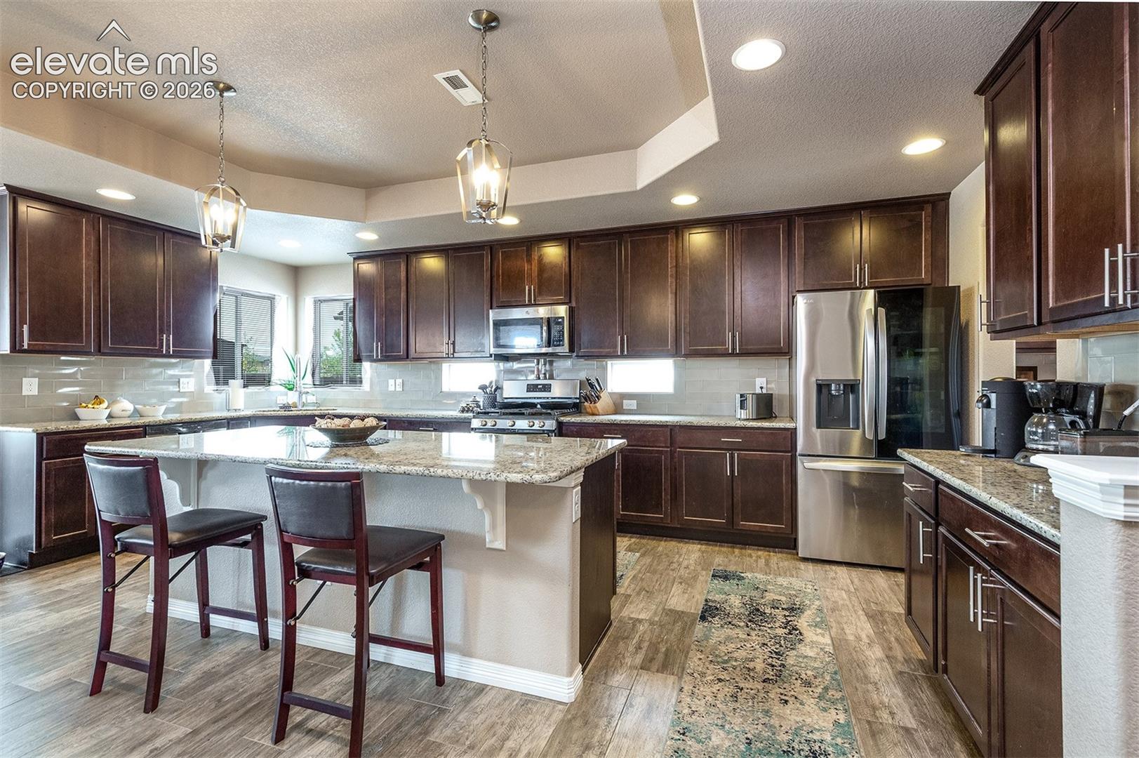 The kitchen is a chef’s delight, featuring upgraded 42” cabinetry, granite countertops, custom backsplash, large central island with breakfast bar, walk-in butler’s pantry, and stainless steel appliances