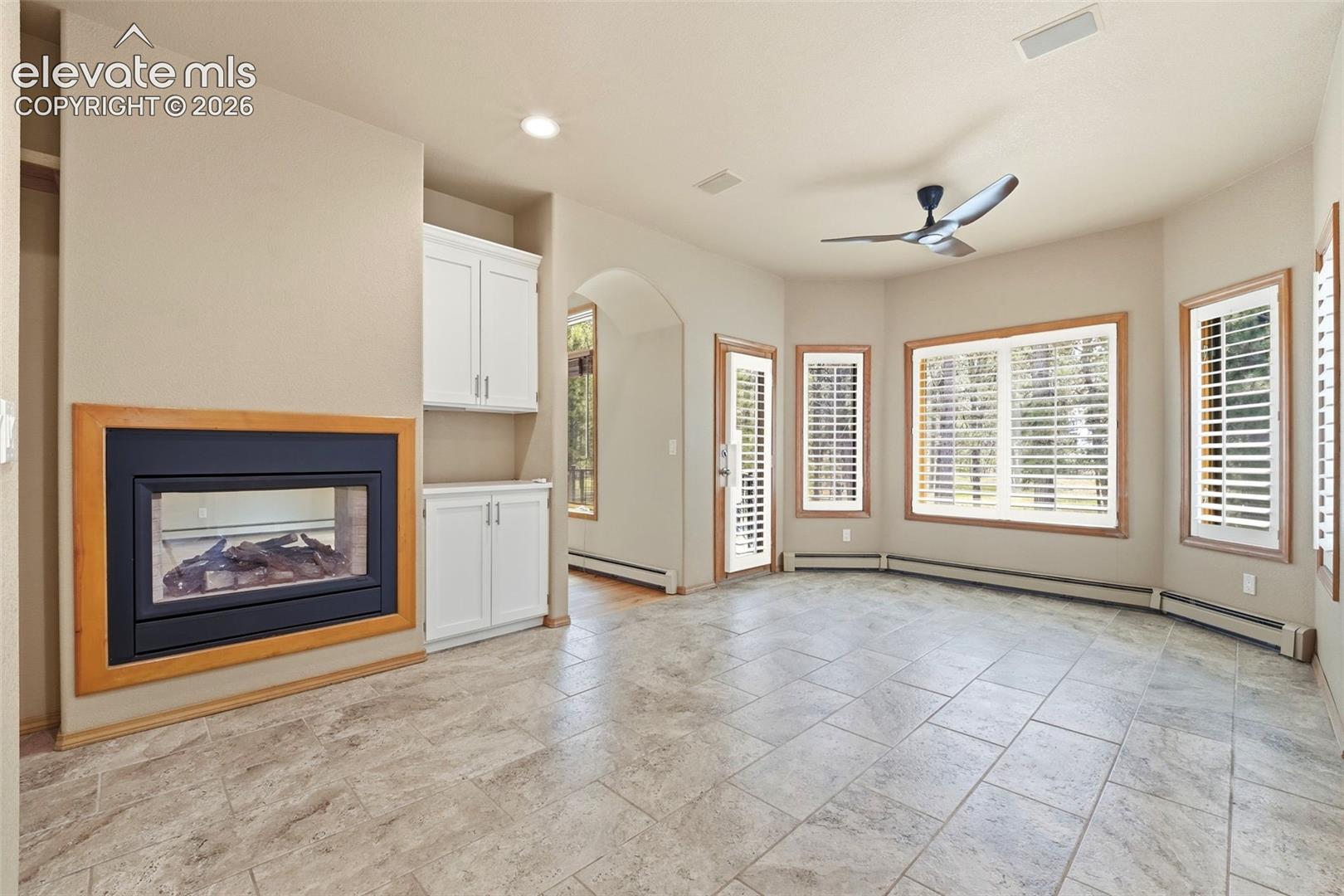 Spacious room featuring tile flooring, a built-in fireplace with a wood frame, recessed lighting, and white cabinetry