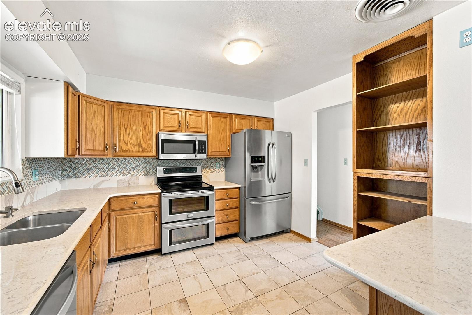 Ceramic tile flooring, light-toned countertops, wood cabinetry, stainless steel appliances, and a mosaic tile backsplash