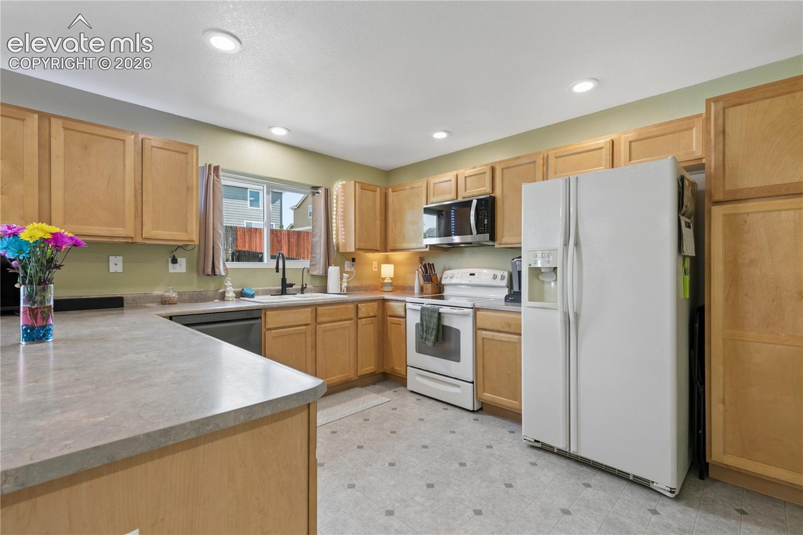 U-shaped kitchen featuring light wood cabinetry, recessed lighting, and a window above the sink