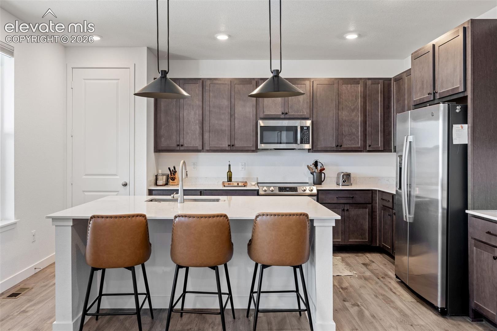 White kitchen island with a built-in sink, dark wood-finish cabinetry, stainless steel appliances, and LVP flooring