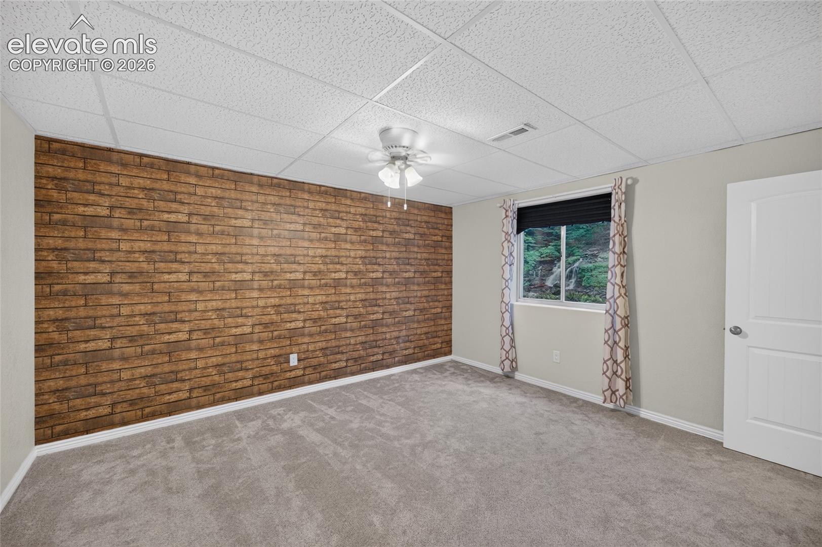 Textured wood-finish accent wall, neutral carpeting, suspended drop ceiling, and ceiling-mounted light fixture