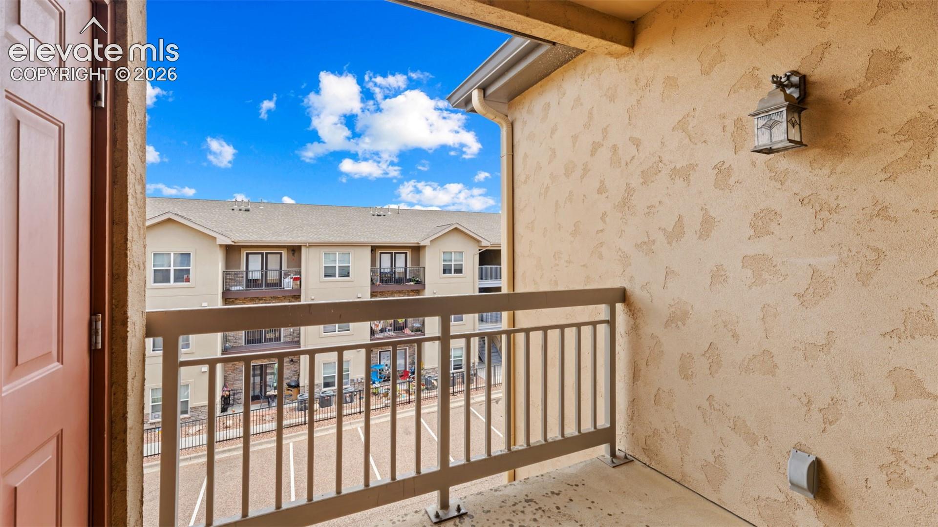 Private balcony featuring a stucco wall, metal railing, and an exterior wall lantern