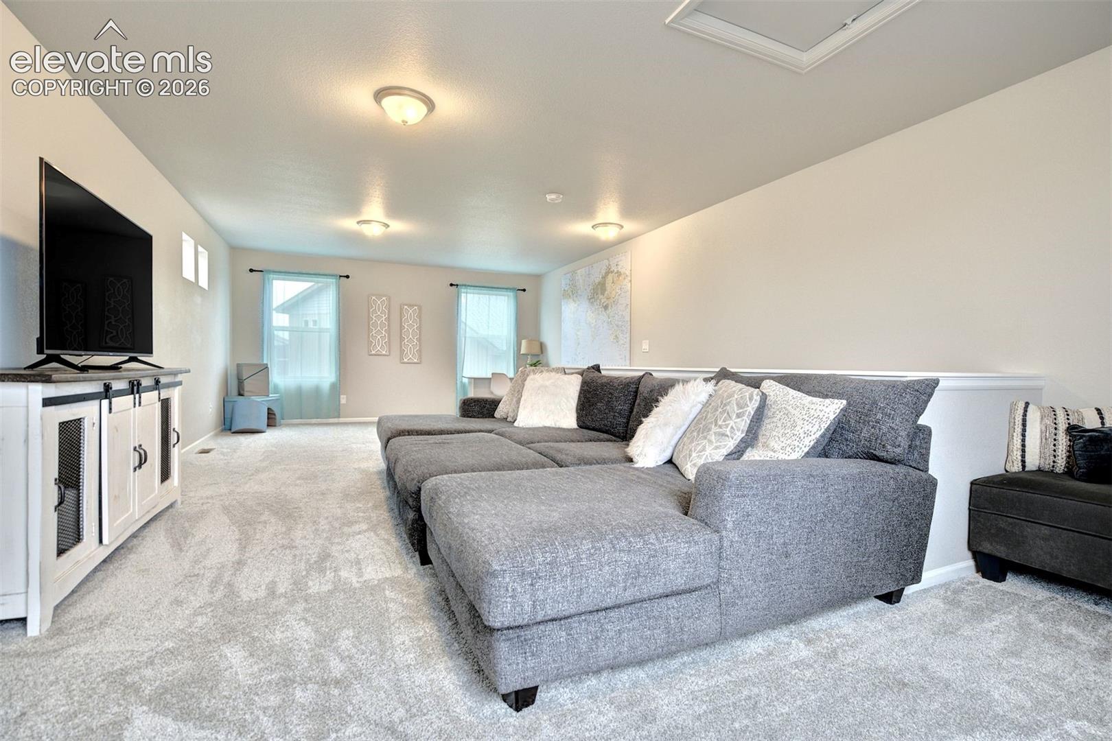 Open-concept room featuring neutral wall paint, wall-to-wall carpeting, flush-mount ceiling lighting, and multiple windows