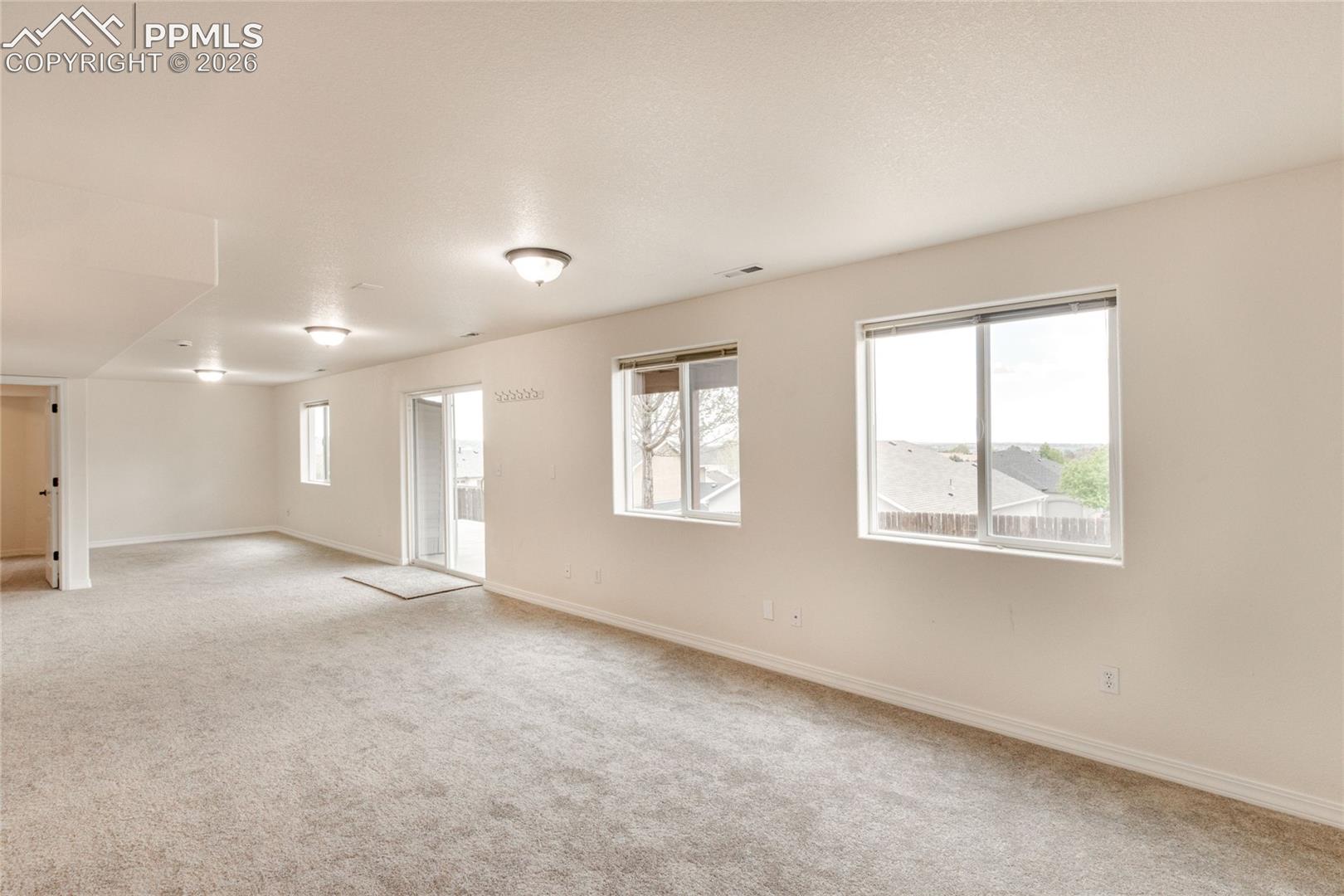 Spacious basement bonus room featuring neutral carpeting, light-toned walls, and a sliding glass door leading to the backyard patio.