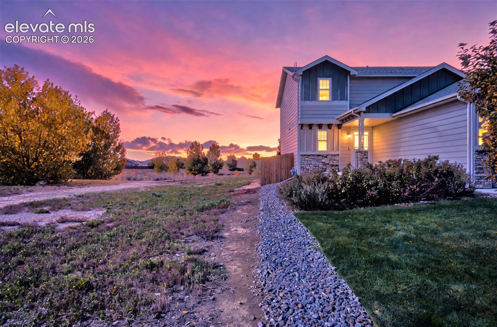 Two-story residence featuring horizontal lap siding, stone veneer accents, an attached garage, a gravel walkway, and a manicured lawn