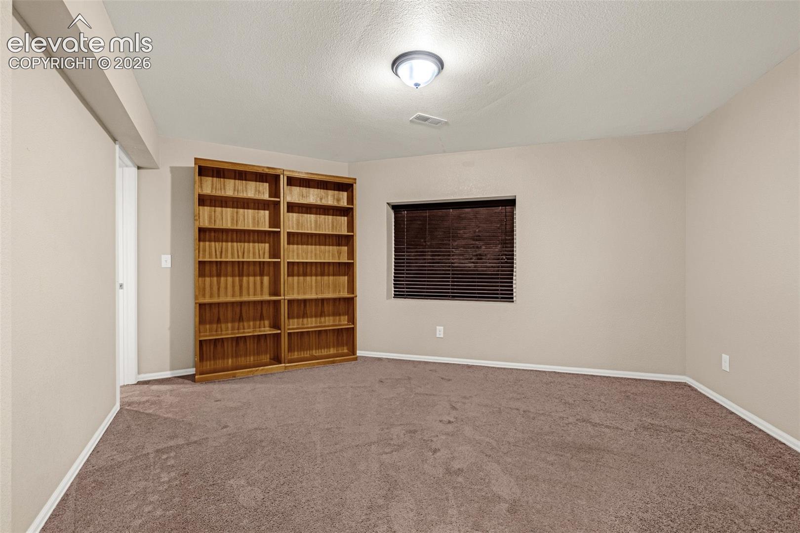 Carpeted flooring, recessed window with blinds, overhead flush mount lighting, and built-in wood-finish shelving
