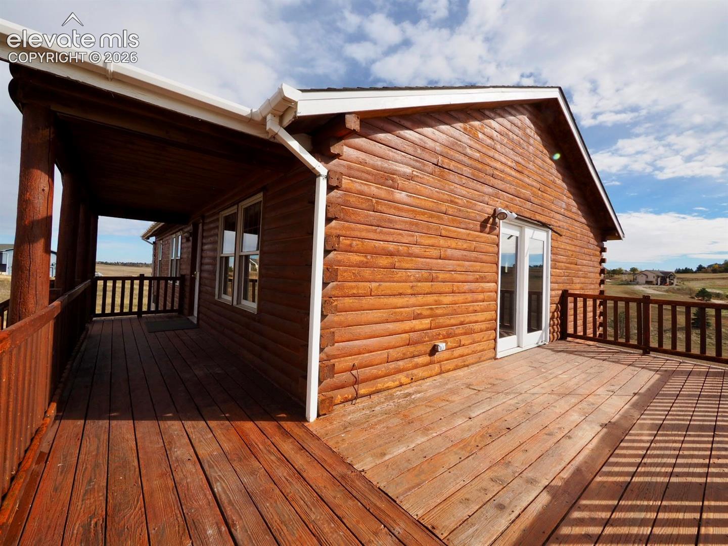 Log exterior cabin featuring a wrap-around wooden deck, integrated covered porch, and double-glass patio doors