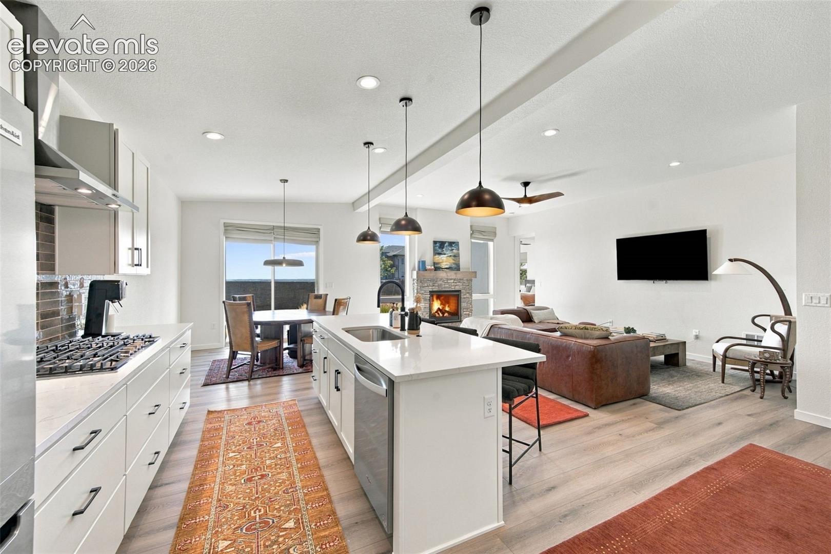 Kitchen featuring a central island with quartz countertops, stainless steel appliances, wood-finish flooring, recessed lighting, and a stone-clad fireplace