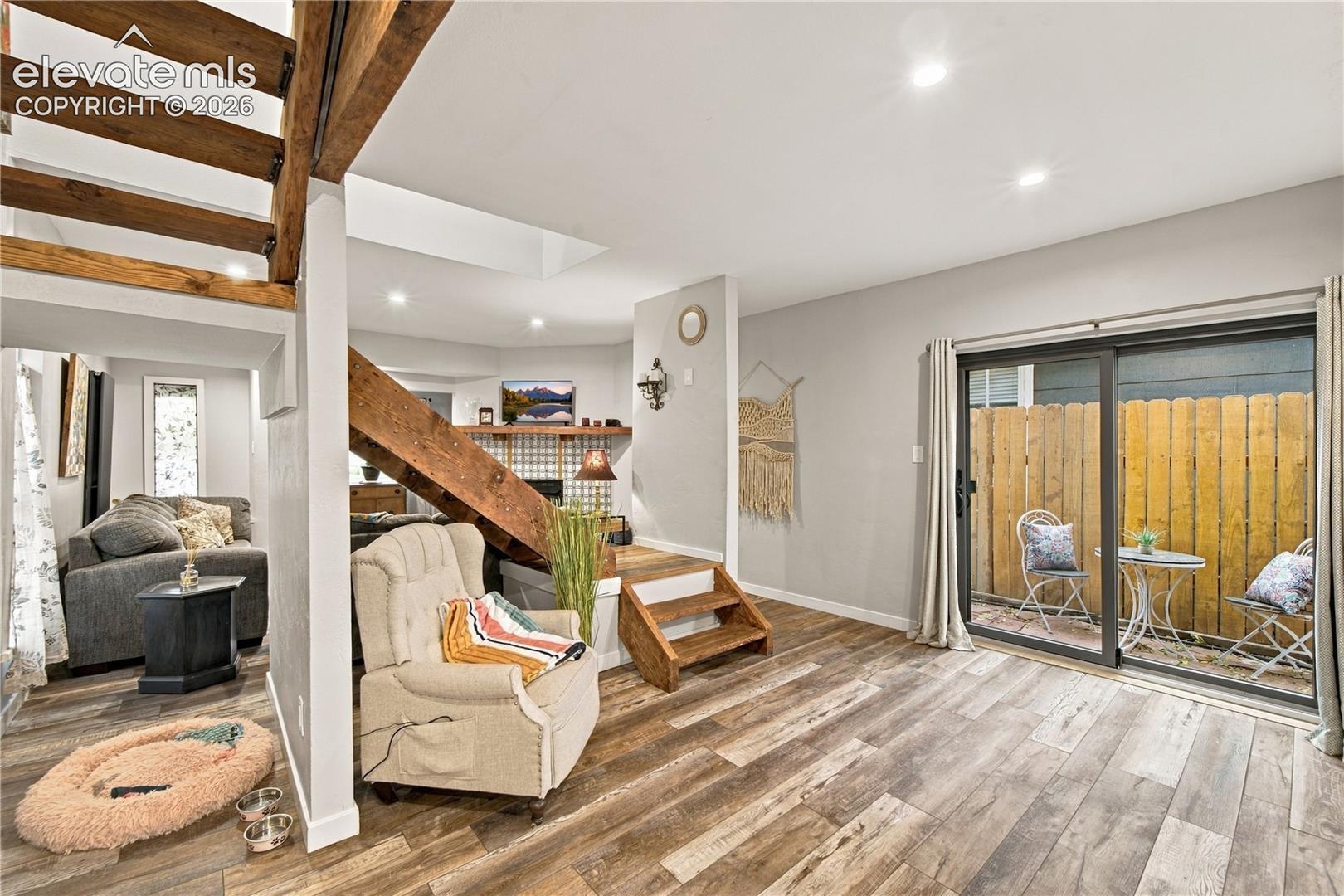 Open-concept interior featuring wood-finish flooring, exposed wood stair stringers, recessed lighting, and sliding glass doors with access to a fenced outdoor area