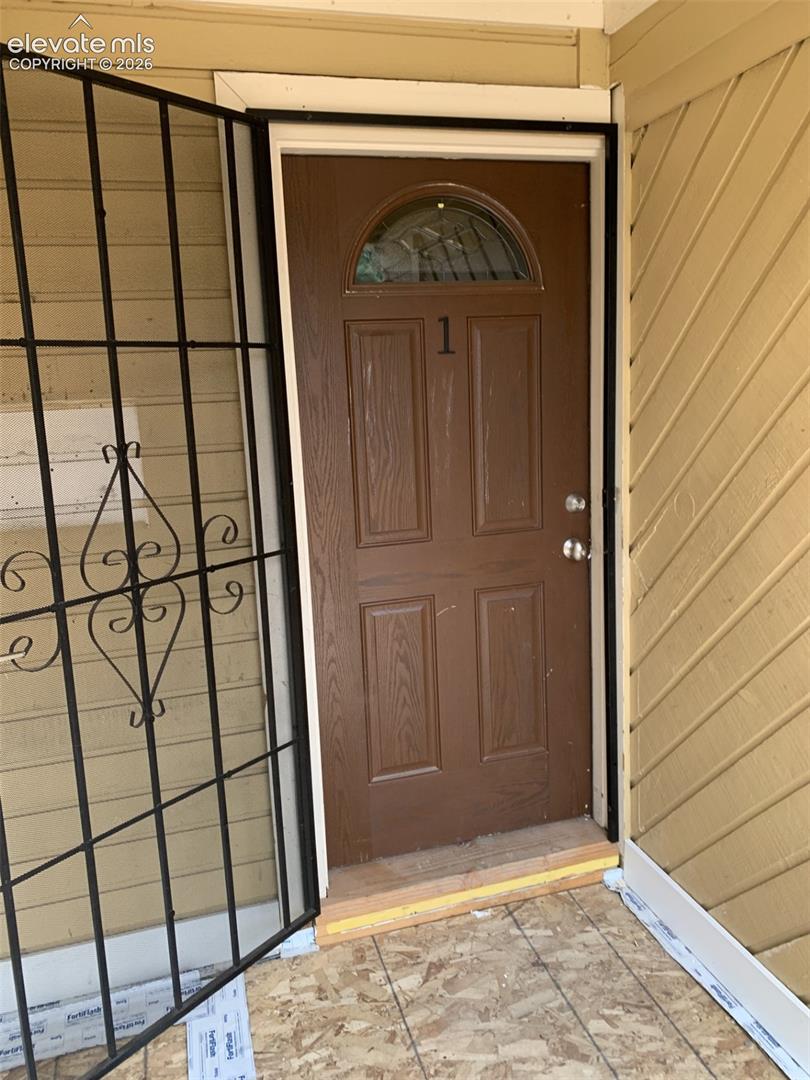 Brown entry door with an arched glass insert, featuring an ornamental security gate